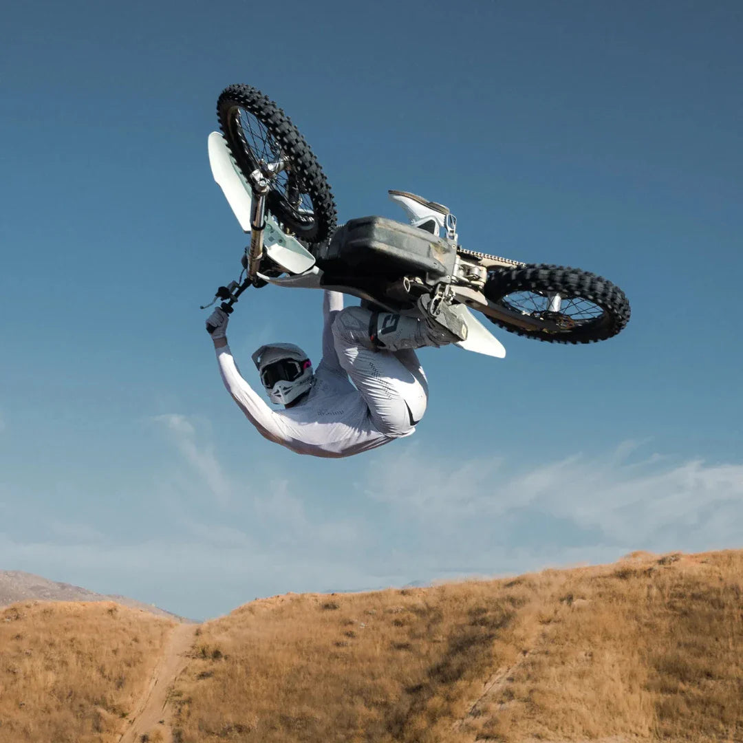 A rider is performing a trick on a Stark Varg electric motocross bike with a clear sky in the background.