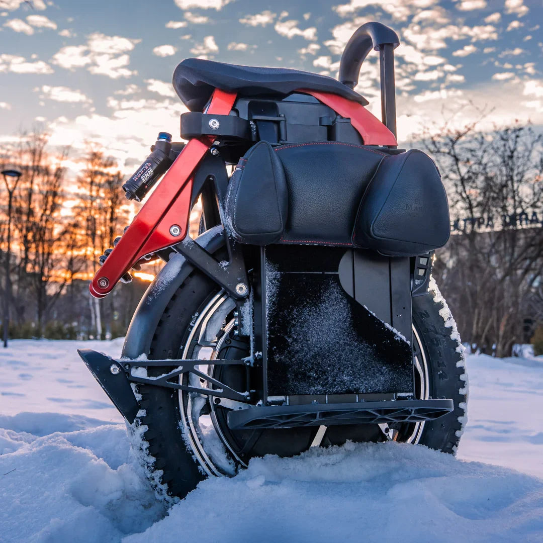 The product in the image is an electric unicycle, model KingSong S22 Pro. The image shows the rear part of the unicycle, which has a wide tire and a comfortable seating surface. In the background, a snowy landscape and sunset are visible, creating a picturesque ambiance. The unicycle is equipped with a suspension system, indicating a comfortable ride.