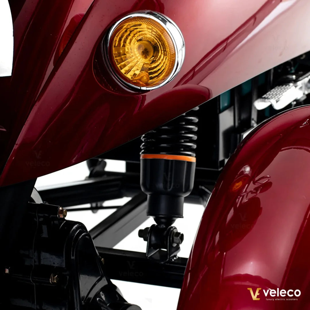 Izdelek je električni mobilni voziček, model Veleco ZT63. Na sliki je vidna del strukture vozička, vključno z rumenim smernikom in delom vzmetenja. Barva vozička je rdeča, kar daje moderni in privlačni videz. Vidna je tudi črna podlaga, ki podpira konstrukcijo.