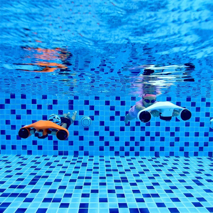 The product in the image is an electric underwater scooter, brand Asiwo, model Manta. We see two children diving in a pool, each with a different scooter – one is orange, the other is white. Both devices are designed for easy underwater movement and provide a fun experience exploring the underwater world. The pool has blue tiles, creating a pleasant aquatic environment.