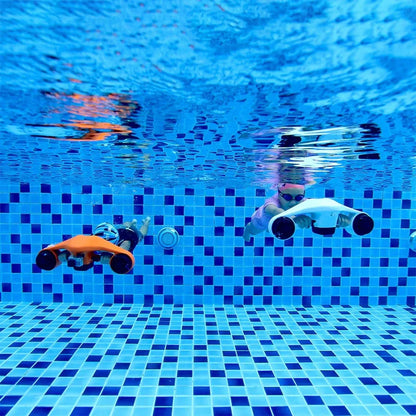 The product in the image is an electric underwater scooter, brand Asiwo, model Manta. We see two children diving in a pool, each with a different scooter – one is orange, the other is white. Both devices are designed for easy underwater movement and provide a fun experience exploring the underwater world. The pool has blue tiles, creating a pleasant aquatic environment.