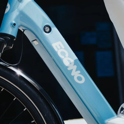 The product in the image is an Econo electric bike, model Mare City. The image shows part of the bike's frame in light blue, clearly displaying the Econo logo. The battery, integrated into the frame, is also visible, giving the bike a sleek and modern look. The bike's design suggests it is intended for city riding.