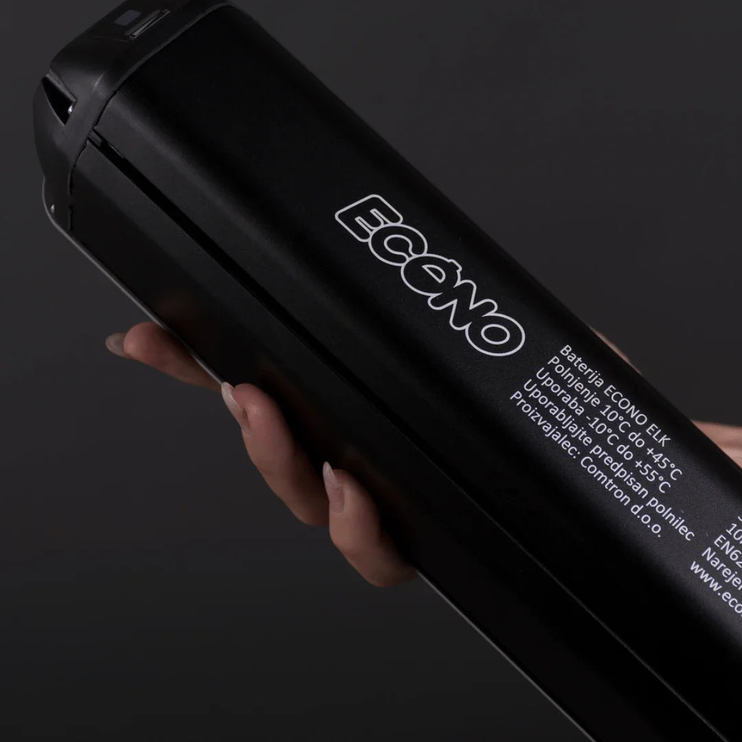 Izdelek je električno kolo, znamka je Econo, model pa je Pantera C9. Na sliki je vidna baterija, ki jo drži roka, z jasno označenim logotipom Econo. Baterija je črne barve in vsebuje informacije o polnjenju ter delovnih temperaturah.
