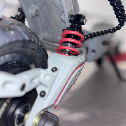 Izdelek je električni skiro, model Eco Speed 10X V2. Na sliki je prikazana podrobnost vzmetenja skiroja, kjer so vidni rdeči vzmeti ter del okvirja, ki podpira zadnje kolo. Vzmetenje je zasnovano za boljšo udobnost pri vožnji, kar je pomembno za stabilnost in nadzor.