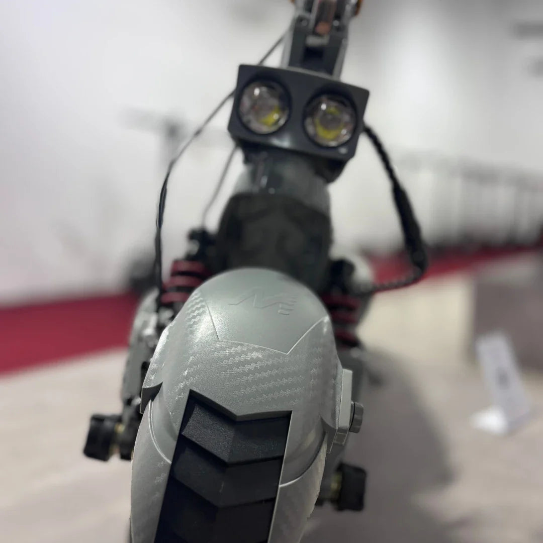 Izdelek na sliki je električni skiro, model Eco Speed 10X V2. Na sliki je vidna sprednja stran skiroja, ki ima dva svetlobna vira, kar nakazuje na možnost vožnje v slabših svetlobnih pogojih. Vidna je tudi podrobnost na zadnjem delu, ki vključuje gumijast profil kolesa in vzmetenje, kar prispeva k udobni vožnji.