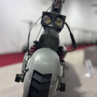 Izdelek na sliki je električni skiro, model Eco Speed 10X V2. Na sliki je vidna sprednja stran skiroja, ki ima dva svetlobna vira, kar nakazuje na možnost vožnje v slabših svetlobnih pogojih. Vidna je tudi podrobnost na zadnjem delu, ki vključuje gumijast profil kolesa in vzmetenje, kar prispeva k udobni vožnji.