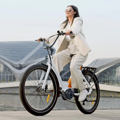 The product is an Electric bike of the Engwe brand, model P275 ST. The image shows a woman riding the bike by the water, dressed in light clothing. The bike features wide tires and a modern design, suggesting a comfortable ride. Contemporary architectural structures are visible in the background.