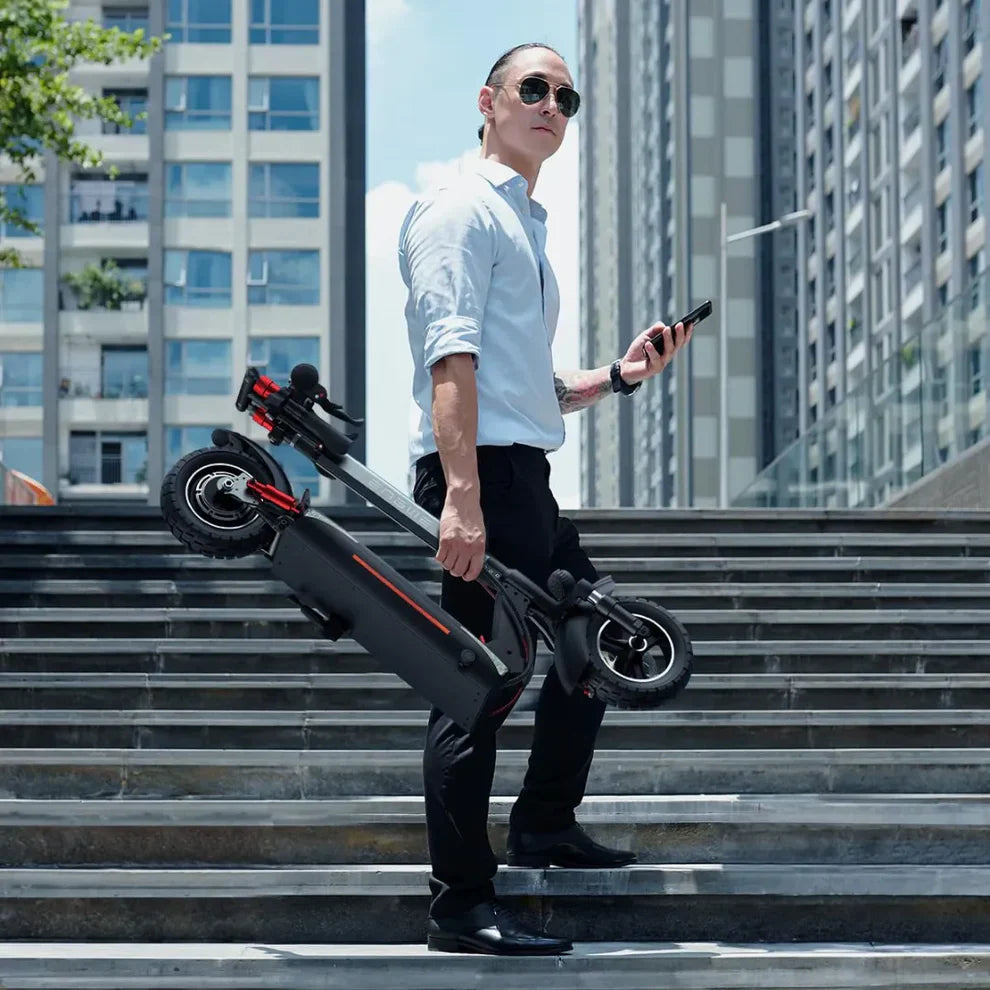 The image shows an Electric Scooter by Engwe, model Y600S. We see a man in a business suit holding a folded scooter and a phone, standing on stairs in an urban setting. The surroundings are modern, with tall buildings in the background, indicating a city environment.