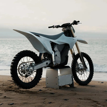 Electric Motocross Motorcycle Stark Varg parked on a sandy beach with ocean waves in the background.