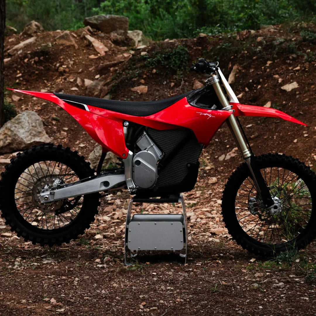 Electric Motocross Stark Varg in red, parked on rocky terrain with greenery in the background.
