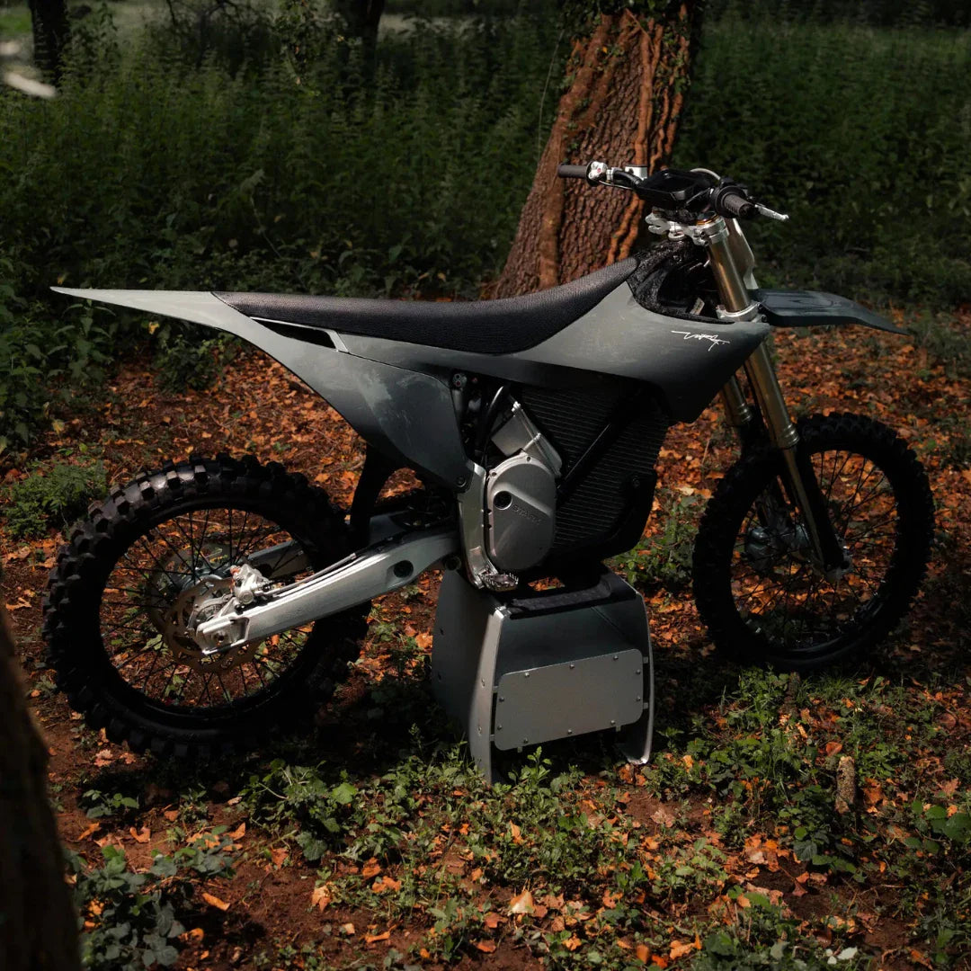 Electric motocross Stark Varg parked among trees and foliage in a wooded area.