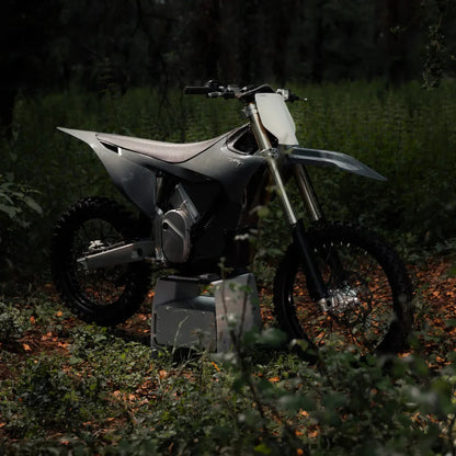 Electric Motocross Stark Varg in a forest environment, surrounded by greenery and fallen leaves.