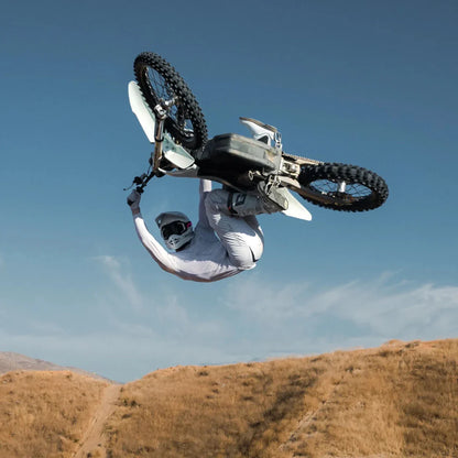 A rider is performing a trick on a Stark Varg electric motocross bike with a clear sky in the background.