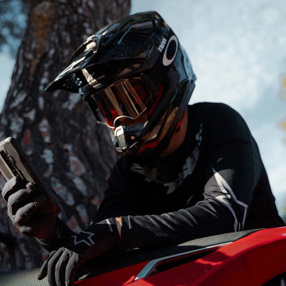 A rider in a black helmet checks their phone next to a Stark Varg electric motocross bike.