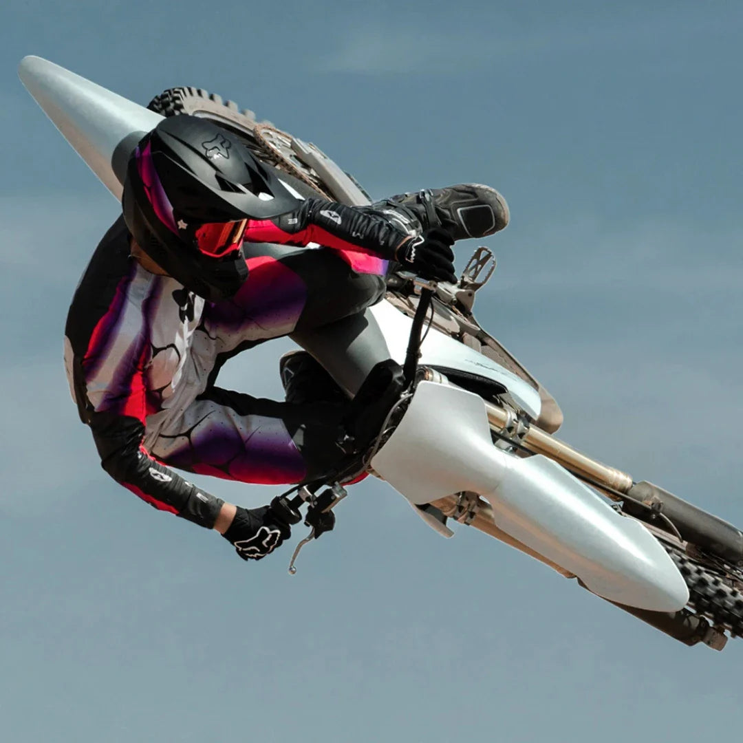 A rider performs a trick with a Stark Varg electric motocross bike against a clear sky background.