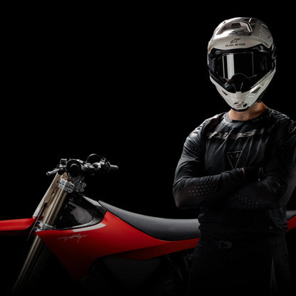 A rider with a helmet stands confidently next to a Stark Varg electric motocross bike.
