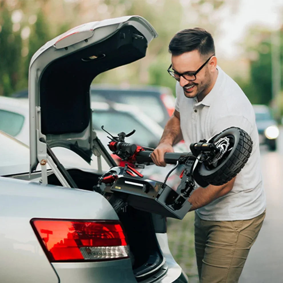 The image shows an electric scooter, model Engwe Y600S. A man is seen loading it into the trunk of a car. He is holding it carefully and smiling, which suggests he is happy with the scooter. In the background, there are other cars, indicating an urban environment.
