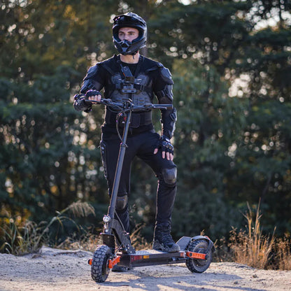 The image shows an Electric Scooter, model Joyor S10 S-Z. The person on the scooter is wearing protective gear, including a helmet and protective clothing, suggesting use in more demanding conditions. The background is natural, indicating the scooter is suitable for riding on various terrains.