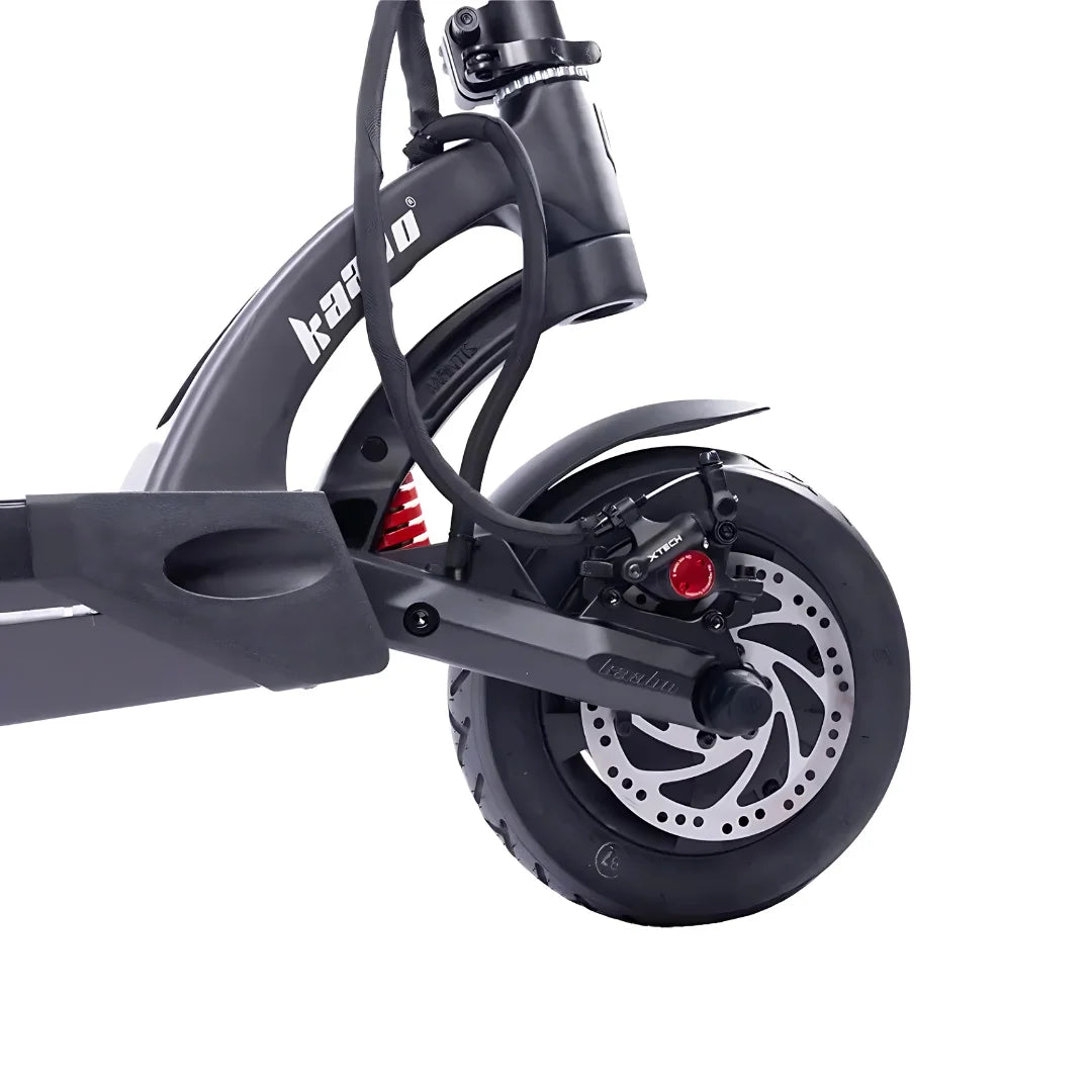 The image shows an Electric scooter from the brand Kaabo, model Mantis 10 Plus. The scooter's rear wheel is visible, featuring disc brakes and a wide tire. It is also equipped with a shock absorber, indicating a comfortable ride. The color scheme is dark grey, giving it a modern look.