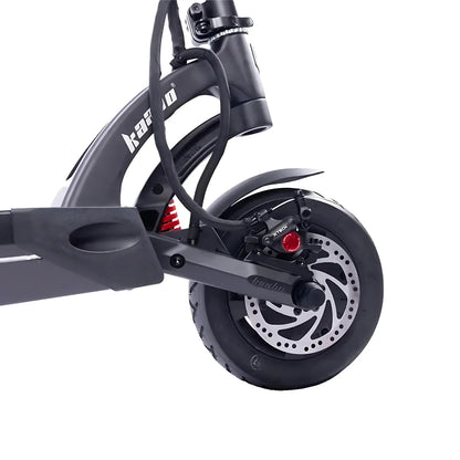 The image shows an Electric scooter from the brand Kaabo, model Mantis 10 Plus. The scooter's rear wheel is visible, featuring disc brakes and a wide tire. It is also equipped with a shock absorber, indicating a comfortable ride. The color scheme is dark grey, giving it a modern look.