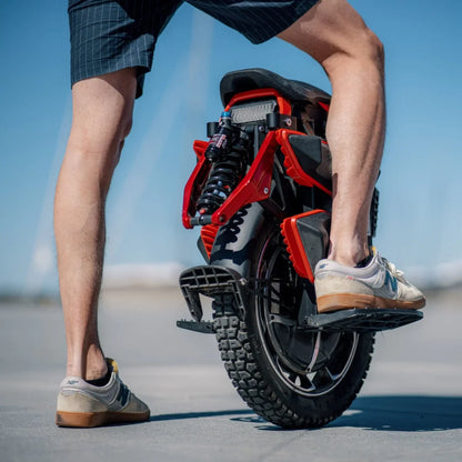 The product is an electric unicycle, KingSong model S22 Pro. The image shows the rear of the unicycle, which features a robust tire and suspension. The person standing next to it is wearing shorts and athletic shoes, suggesting a relaxed and active use of this mode of transport. In the background, there's a clear sky, creating a pleasant atmosphere.
