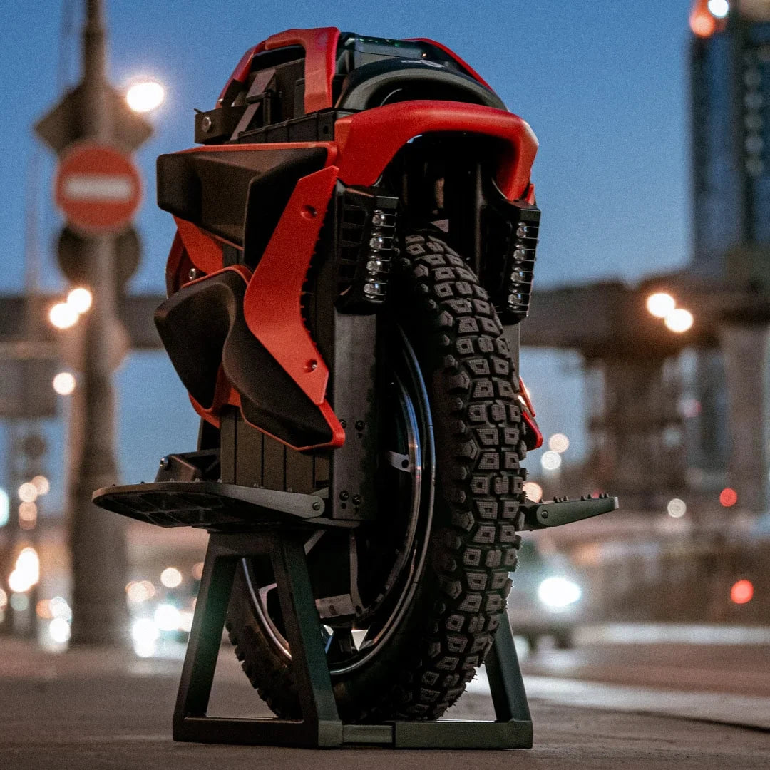The product pictured is an electric unicycle, model KingSong S22 Pro. The unicycle is shown in red and black, placed on a stand. A large tire with a prominent tread is visible, indicating good grip, along with details on the unicycle's body, which include sculpted lines and LED lights. The background depicts an urban environment with streetlights and traffic signs.