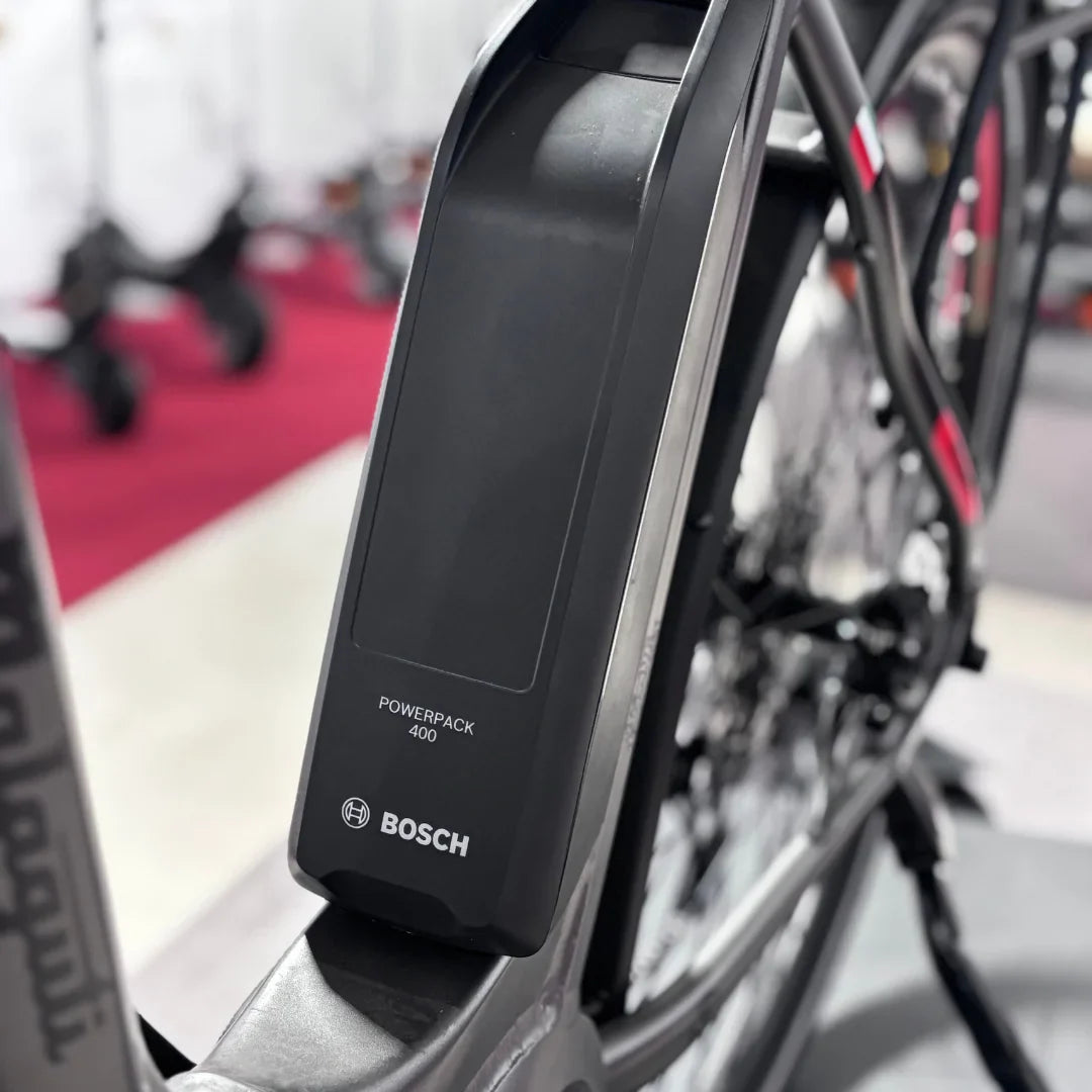 The product in the image is a Malaguti electric bike, model Bolonina. The image shows a Bosch Powerpack 400 battery mounted on the bike's frame. The bike's features suggest a modern design and technology, which is typical for electric bikes. Other bikes are also visible in the background, indicating the environment where the product is displayed.