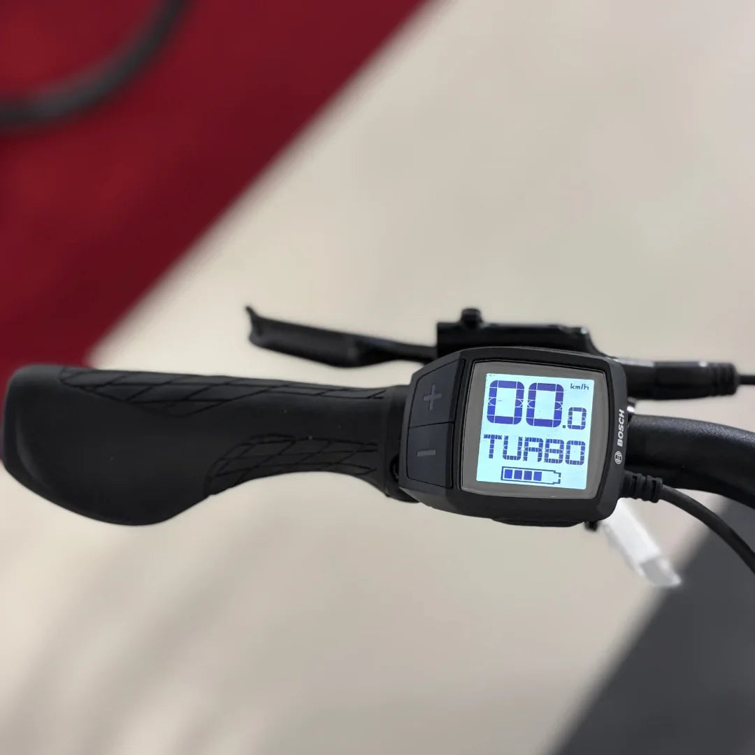 The image shows an Electric bike by Malaguti, model Bolonina. The handlebars with a display showing speed and riding mode (Turbo) are visible. The display features buttons for adjusting speed and modes, allowing for easy control while riding.