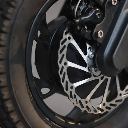 The product is an Electric Scooter, model Mijo MT01. The image shows a part of the wheel, where a stainless steel disc brake, designed for effective braking, is visible. The wheel is surrounded by tires, which provide stability and grip during the ride.