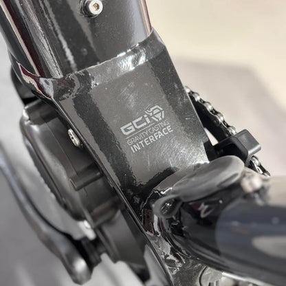 The product is an electric bike, brand Raymon, model GravelRay E 7.0. The image shows the bottom bracket of the bike, where the "Gravity Casting Interface" system is highlighted. Details such as part of the motor and its connection to the chain are also visible, indicating the bike's robust construction.