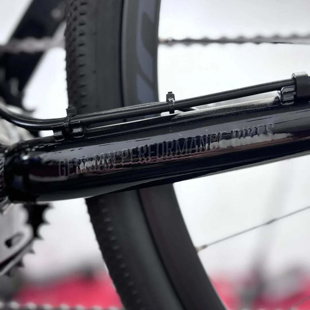 The product is an Electric bike, Raymon brand, model GravelRay E 7.0. The image shows a part of the bike frame, which is black, with visible details such as cables and gears. The equipment indicates high-quality manufacturing, typical of this brand. The bike is designed for riding on gravel surfaces and offers good performance.