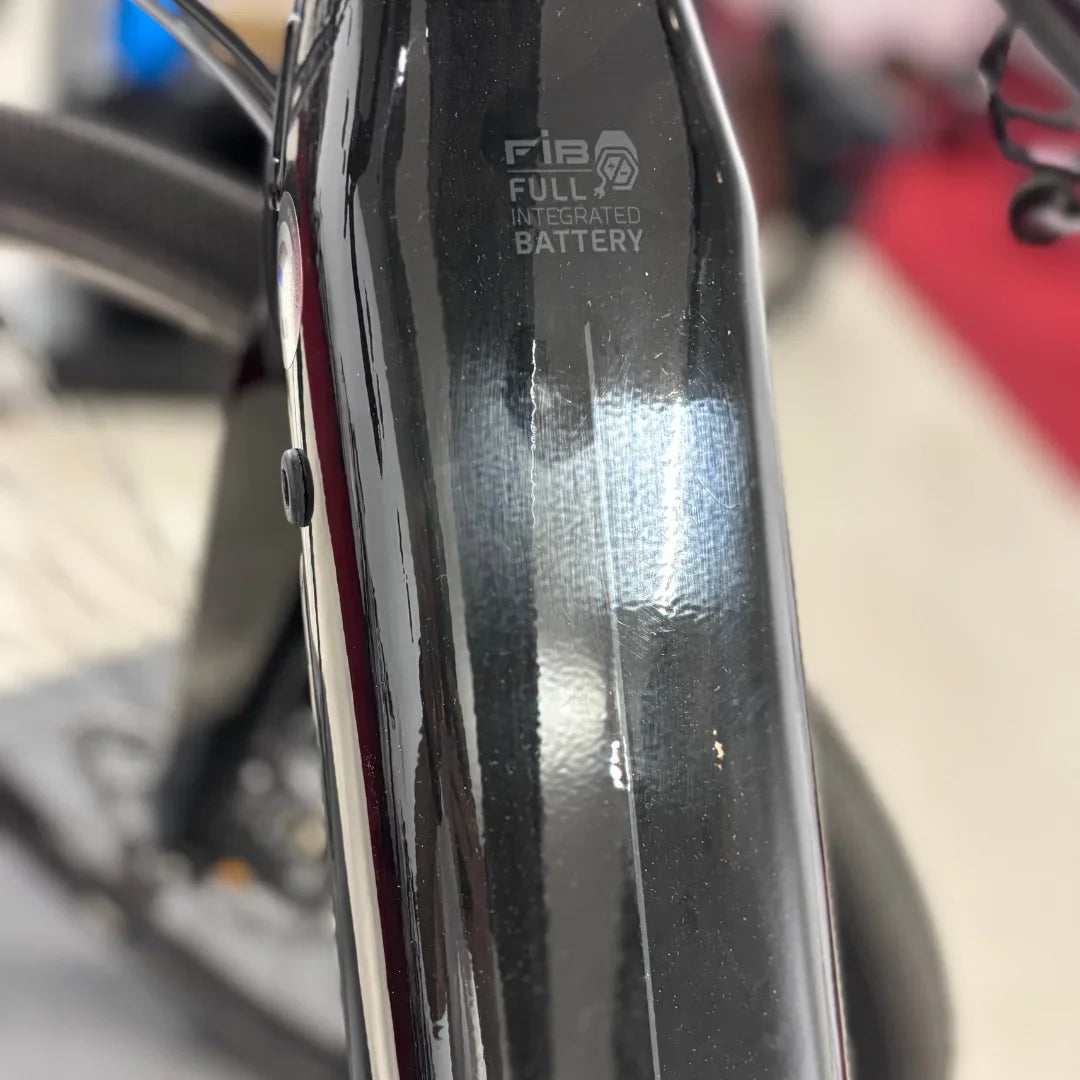 The image shows a Raymon brand electric bike, model GravelRay E 7.0. The battery is fully integrated into the bike's frame, giving the bike an elegant appearance. The bike has a black color and a modern design, which is characteristic of this type of electric model.