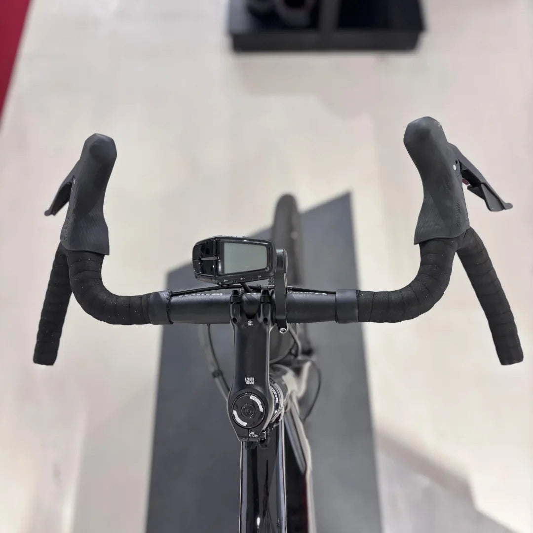 The product is an Electric bike, brand Raymon, model GravelRay E 7.0. The image shows the front part of the handlebars, which feature sporty grips and a digital display, likely for showing ride information. The bike also has a sleek black color and is designed for gravel riding.