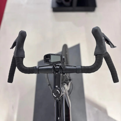 The product is an Electric bike, brand Raymon, model GravelRay E 7.0. The image shows the front part of the handlebars, which feature sporty grips and a digital display, likely for showing ride information. The bike also has a sleek black color and is designed for gravel riding.