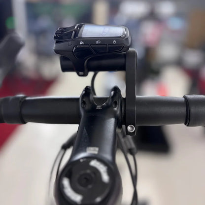 The product is an Electric bike from the brand Raymon, model GravelRay E 7.0. The image shows the bike's handlebars with an attached display, which shows various functions such as riding mode and lighting. The bike has a robust design, typical of gravel bikes, allowing it to be ridden on various terrains.