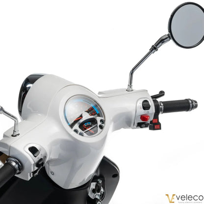 The product is an Electric motorcycle, brand Veleco, model Cristal. The image shows the control panel of the motorcycle, which includes the speedometer, control levers, and mirror. The color combination is white and black, giving the motorcycle an elegant look. Control buttons and details for easy use are also visible.