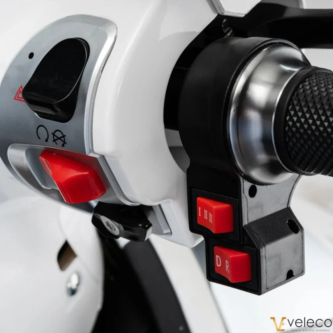 The product in the image is an Electric motorcycle, model Veleco Cristal. The control unit is visible, featuring various buttons for speed and direction control. The speed selection buttons and power switch are marked on the scooter, allowing for easy operation while riding.