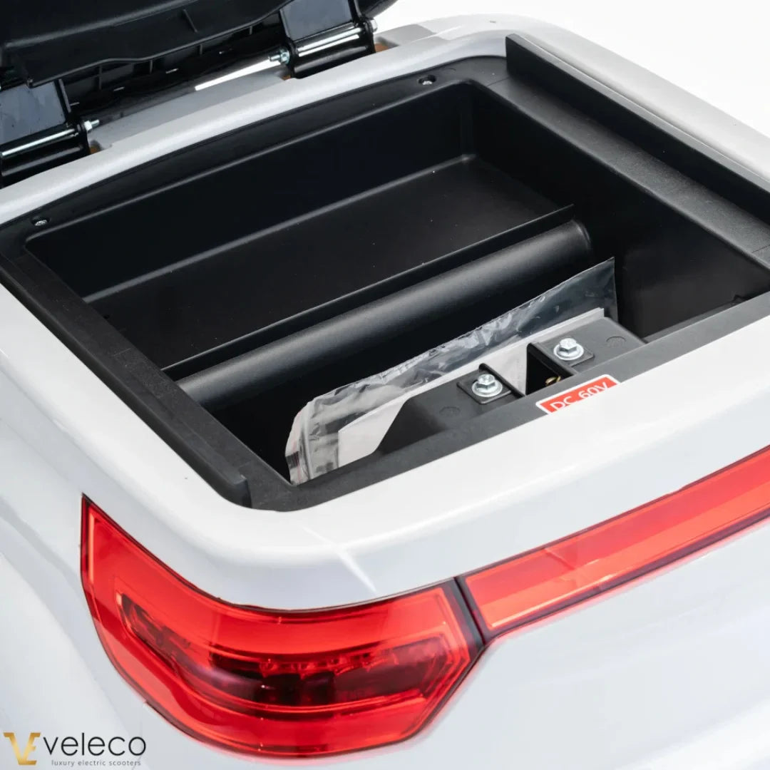 The product is an Electric motorcycle, brand Veleco, model Cristal. The image shows an open storage compartment, revealing the battery and the interior of the scooter. The scooter's tail light is also visible, indicating its design and functionality.