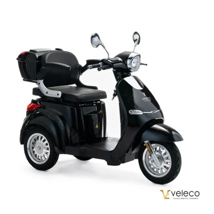 The product pictured is an electric scooter, brand Veleco, model Cristal. The scooter features a sleek black design, a comfortable seating area, and is equipped with front and rear mirrors and a storage compartment at the back. It has three wheels, ensuring stability and easy handling.