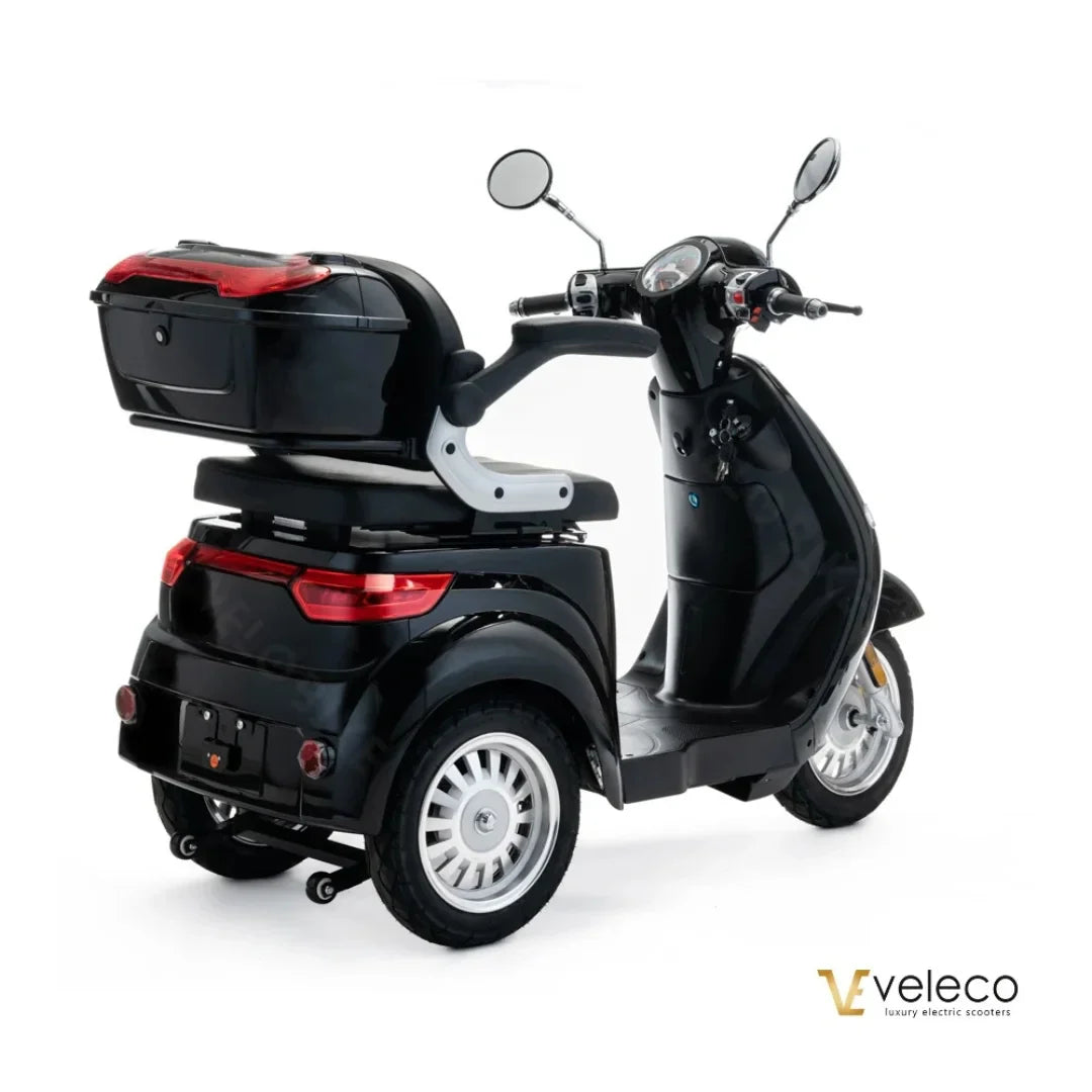 The product pictured is an electric motorcycle, model Veleco Cristal. The motorcycle is black and features a spacious rear trunk for convenient storage. The image also shows mirrors and a control panel, which includes a lock. The motorcycle is designed for comfortable riding and easy handling.