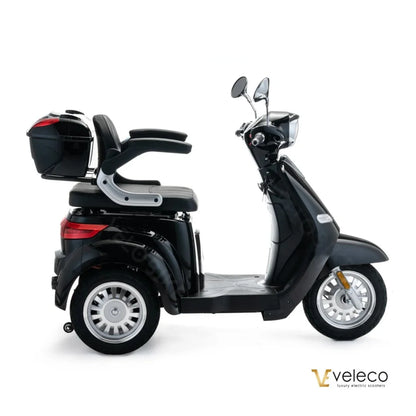 The product is an Electric motorcycle, brand Veleco, model Cristal. The image shows the scooter in black, featuring a comfortable seating area and a spacious trunk at the back. It is equipped with two mirrors and has wide wheels, ensuring stability during the ride.