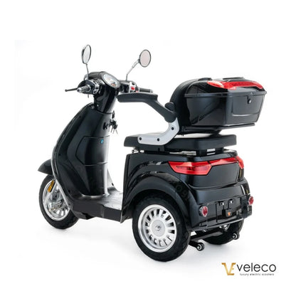 The product is an Electric motorcycle, brand Veleco, model Cristal. The image shows a black three-wheeled scooter with a comfortable seat and a rear luggage rack. Mirrors and gauges are also visible on the handlebars, indicating functionality and comfort during the ride.