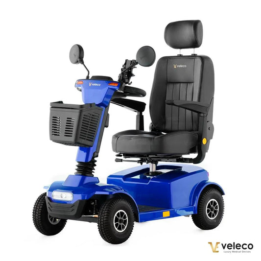 Izdelek na sliki je električni skuter, model Veleco Jumpy. Skuter je zasnovan za udobno vožnjo in ima široko sedežno površino s podloženim naslonjalom ter ročaji za podporo. Na sprednjem delu je košara za shranjevanje, kar povečuje njegovo funkcionalnost. Barva skuterja je svetlo modra, kar mu daje sodoben videz.