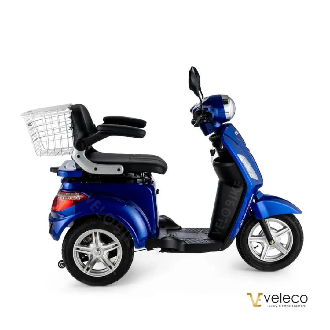 Izdelek na sliki je električni mobilni voziček, model Veleco ZT15. Na sliki je prikazan voziček v modri barvi, ki ima udobno sedežno površino z naslonjalom ter košaro za shranjevanje na zadnjem delu. Ima tri kolesa, kar omogoča stabilno vožnjo, in je zasnovan za enostavno upravljanje.