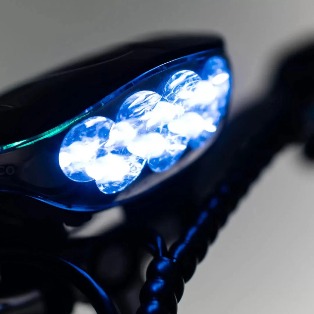 The product is an Electric Mobility Scooter, model Veleco ZT16. The image shows a part of the scooter, illuminated by powerful LED lights located on the front. The lights are blue and designed to improve visibility while riding. The overall design of the scooter is sleek and modern.